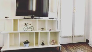 A room with a mounted TV on a white wall, wooden flooring, and a white shelving unit with decorative items. - Le Terrazze apartment, on two floors (Unknown)
