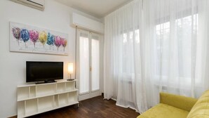 A living room with a flat-screen TV on a white stand, a yellow sofa, and a painting of colorful trees on the wall. - Le Terrazze apartment, on two floors (Unknown)
