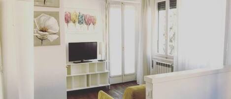 Una sala de estar con una televisión sobre un mueble bajo, un sillón amarillo y un armario blanco.