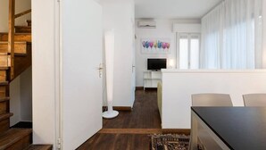 A modern living room with a wooden staircase, a flat-screen TV, and a large window with sheer curtains. - Le Terrazze apartment, on two floors (Unknown)