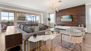 A modern living room with a sofa, coffee table, and ottoman, large windows, and a wooden accent wall.