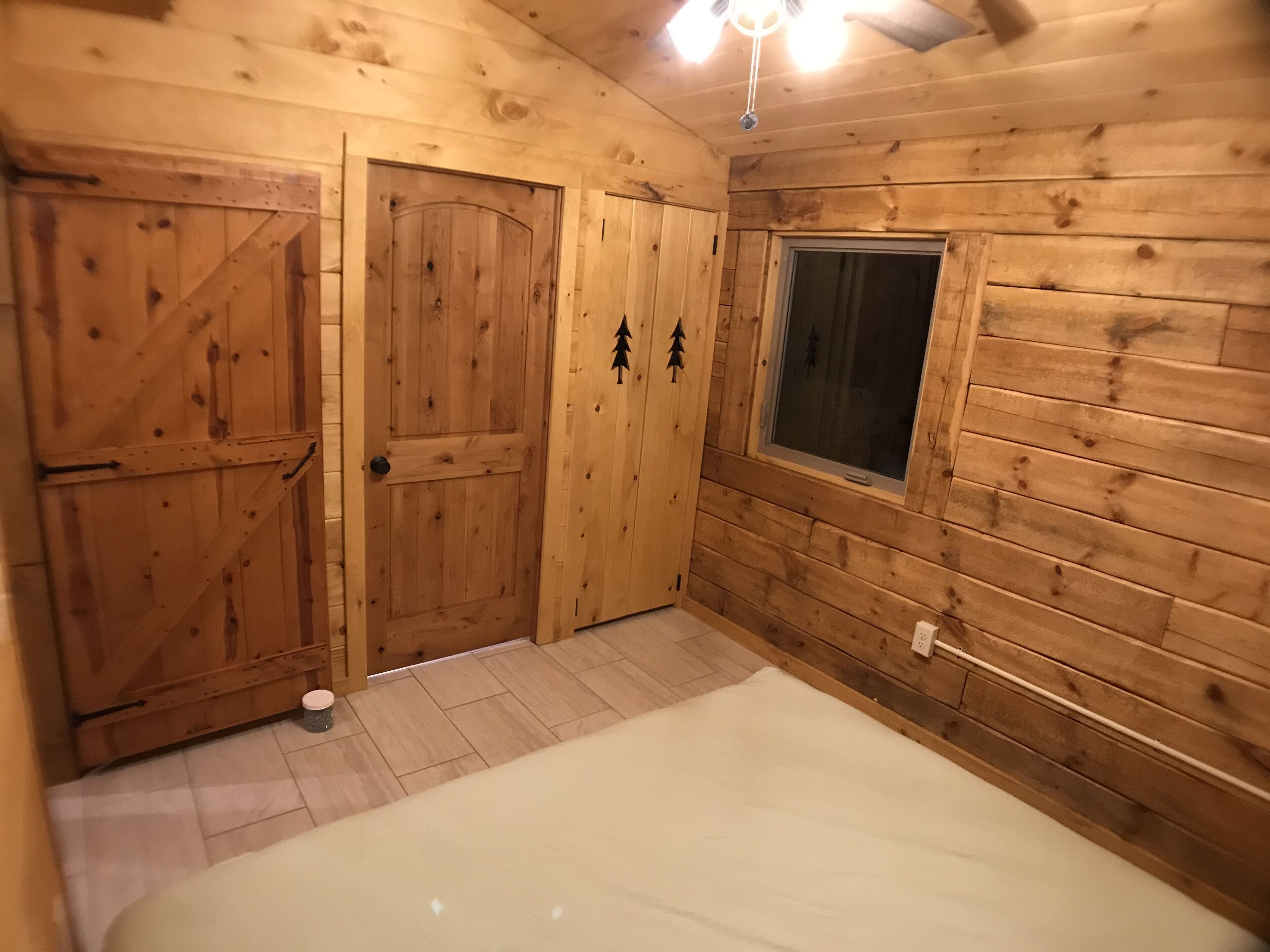 Una habitación de madera con dos puertas, una ventana y una cama.