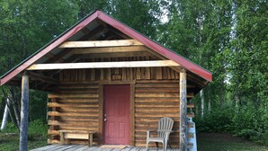 A rustic log cabin with a red door, a wooden bench, and a Adirondack chair on the porch. - Byers Creek Lodge Eagle Cabin in Denali State Park Trapper Creek Alaska (Trapper Creek)