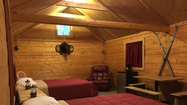 A cozy cabin room with two beds, a wooden ceiling, a small window, a leather chair, and a table. - Byers Creek Lodge Eagle Cabin in Denali State Park Trapper Creek Alaska (Trapper Creek)