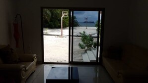 Een woonkamer met een glazen deur die leidt naar een balkon met een basketbalring en uitzicht op de zee.