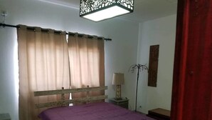 Een slaapkamer met een bed, gordijnen, een nachtkastje, een lamp en een vloerlamp.