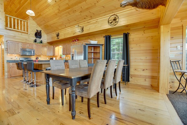 A wooden cabin interior with a dining area, kitchen, and a bear decoration on the ceiling.