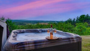 Un bain à remous avec deux verres de vin et une bouteille, le tout placé devant un paysage pittoresque de collines et d’arbres.
