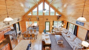 Une cabane en bois spacieuse avec un plafond haut, un coin repas, un salon avec un canapé et une table basse, et une cuisine équipée d’appareils modernes.
