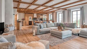 A spacious living room with a wooden ceiling, a grey sofa set, a coffee table, and a fireplace. - Chiemsee Chalet (Frasdorf)