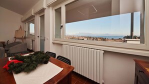 A dining area with a view of a coastal landscape through large windows, a radiator below, and a table with a festive wreath. - Villa Solelago Exclusive (Lonato del Garda)