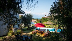 A backyard with a wooden table and chairs, a red umbrella, and a swimming pool. - Villa Solelago Exclusive (Lonato del Garda)