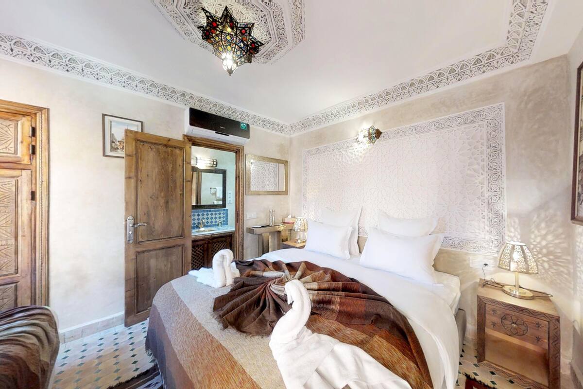 A traditional room with a bed, a wooden wardrobe, a mirror, and a patterned ceiling.