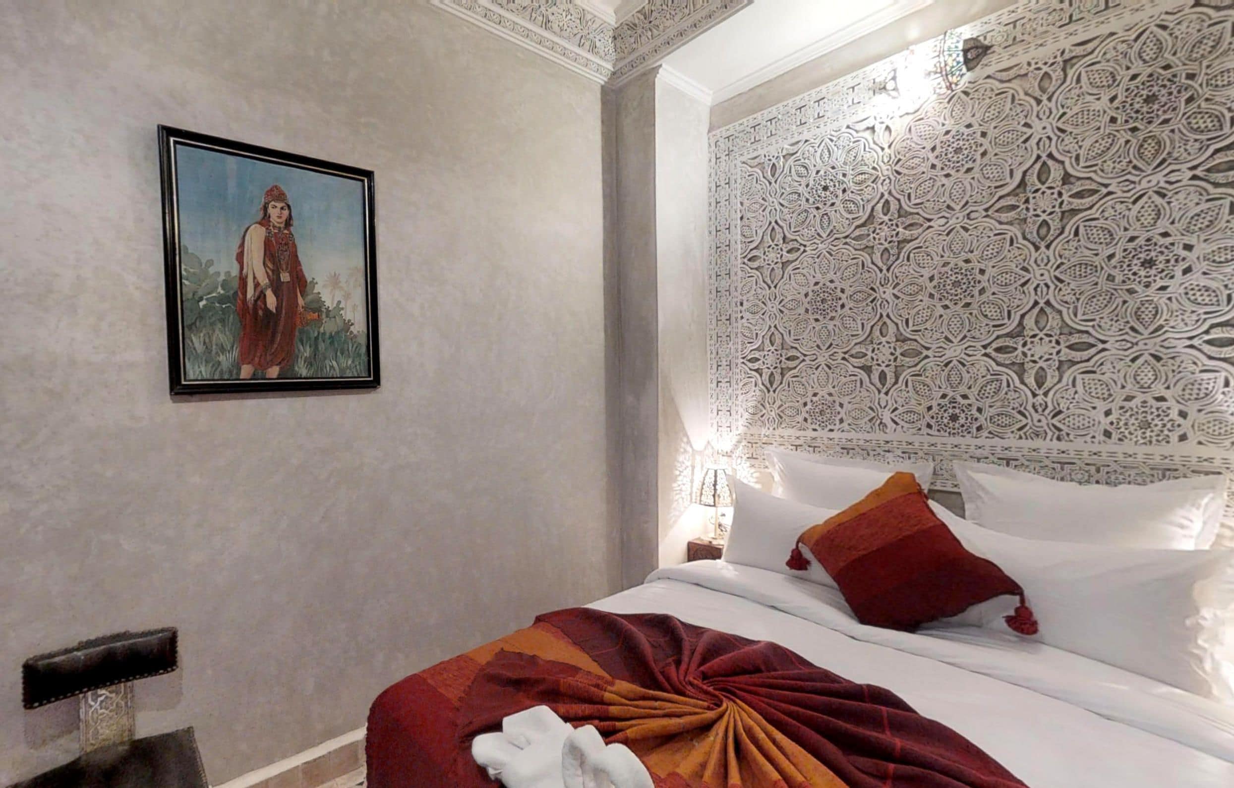 A hotel room with a bed, a framed picture on the wall, and a decorative headboard.