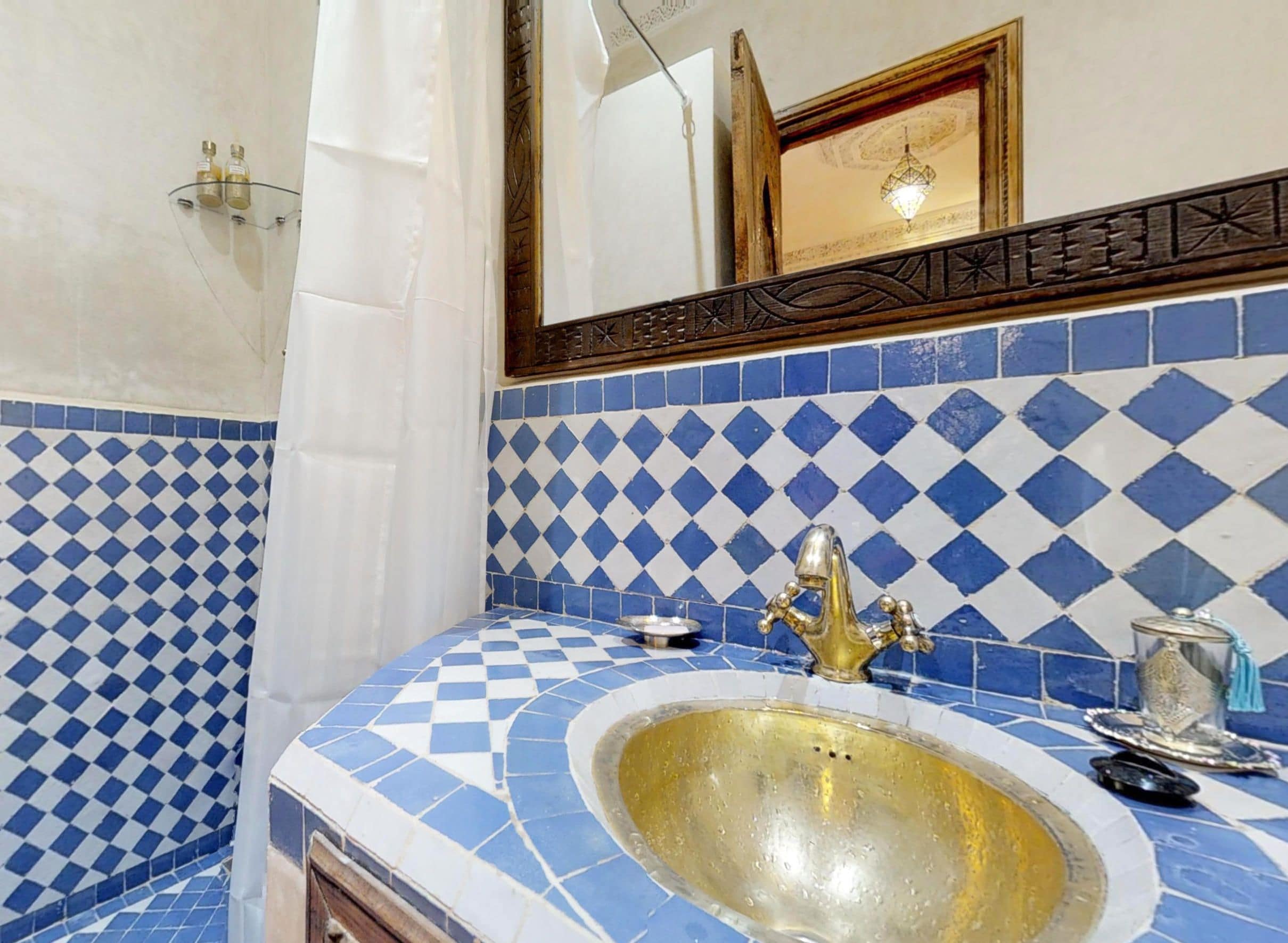 Une salle de bain avec un mur recouvert de carreaux bleus et blancs formant un motif à carreaux, un lavabo doré et un miroir doté d’un cadre décoratif.