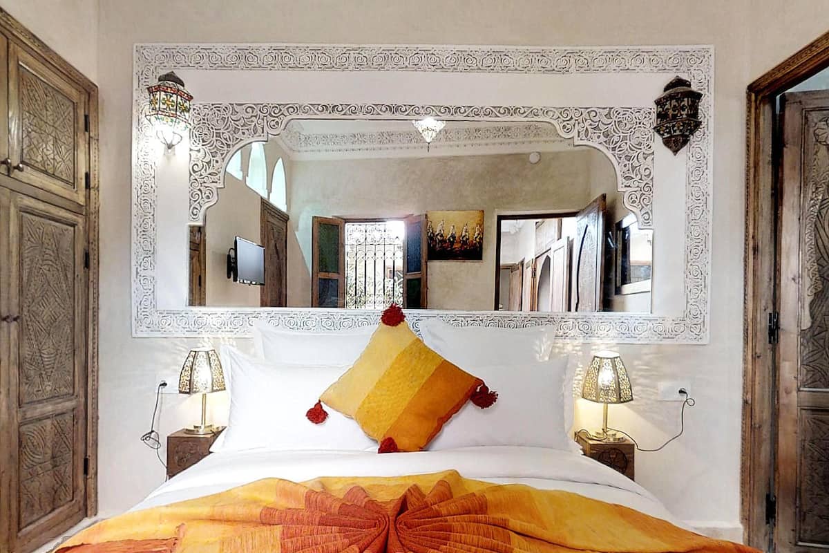 A hotel room with a large ornate mirror above the bed, a patterned bedspread, and two bedside lamps.