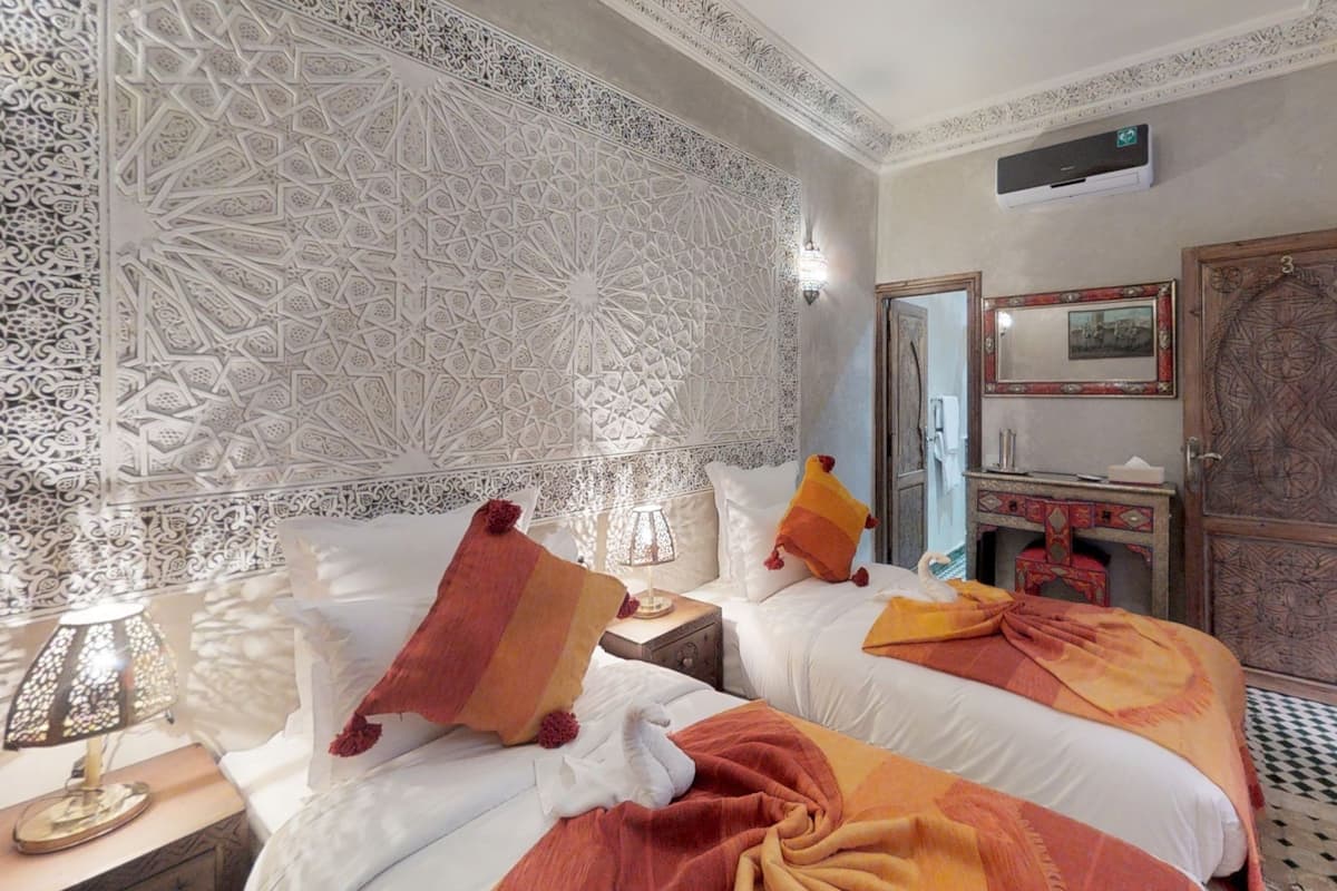 A hotel room with two beds, a decorative wall, a nightstand with a lamp, a dresser, and a mirror.