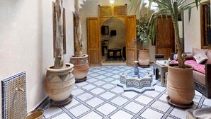 Un interno tradizionale con pavimento piastrellato, grandi piante in vaso e una porta in legno che dà su un'altra stanza.
