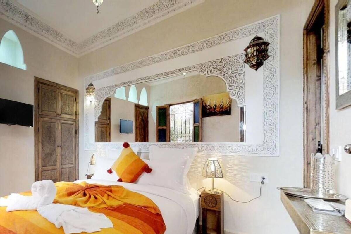 A hotel room with a bed, a mirror, a nightstand, a lamp, and a television.