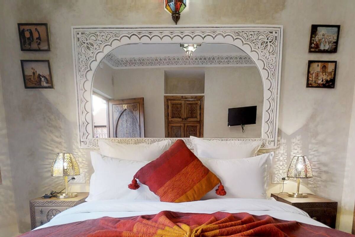 A bed with a large mirror above it, flanked by two nightstands with lamps.
