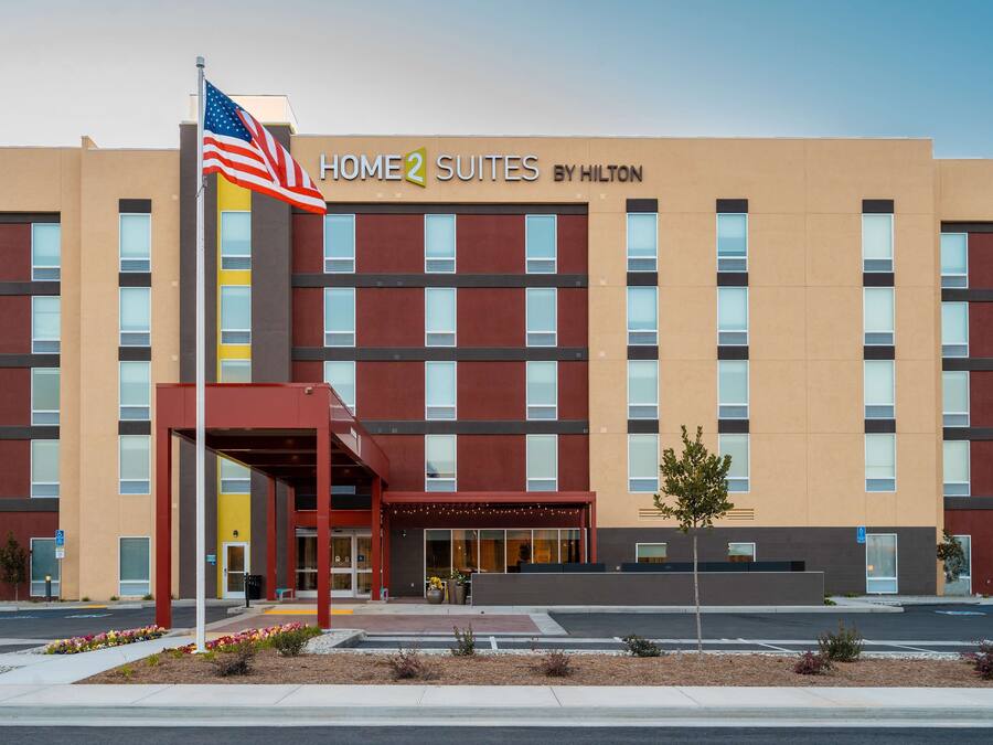 En modern hotellbyggnad med en skylt som visar texten ”HOME 2 SUITES BY HILTON”.