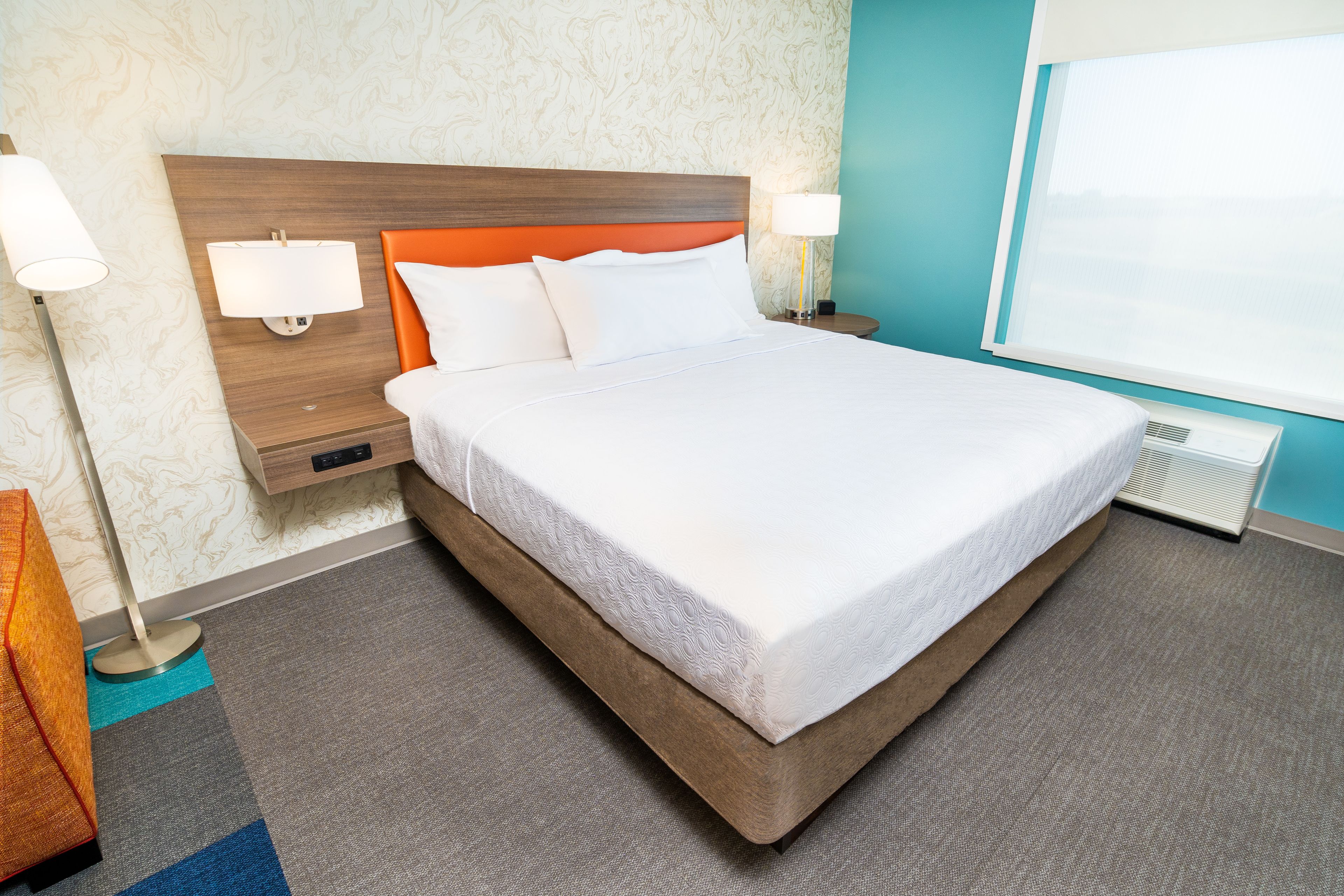 A hotel room with a large bed, two bedside lamps, a nightstand, and a window with a view.