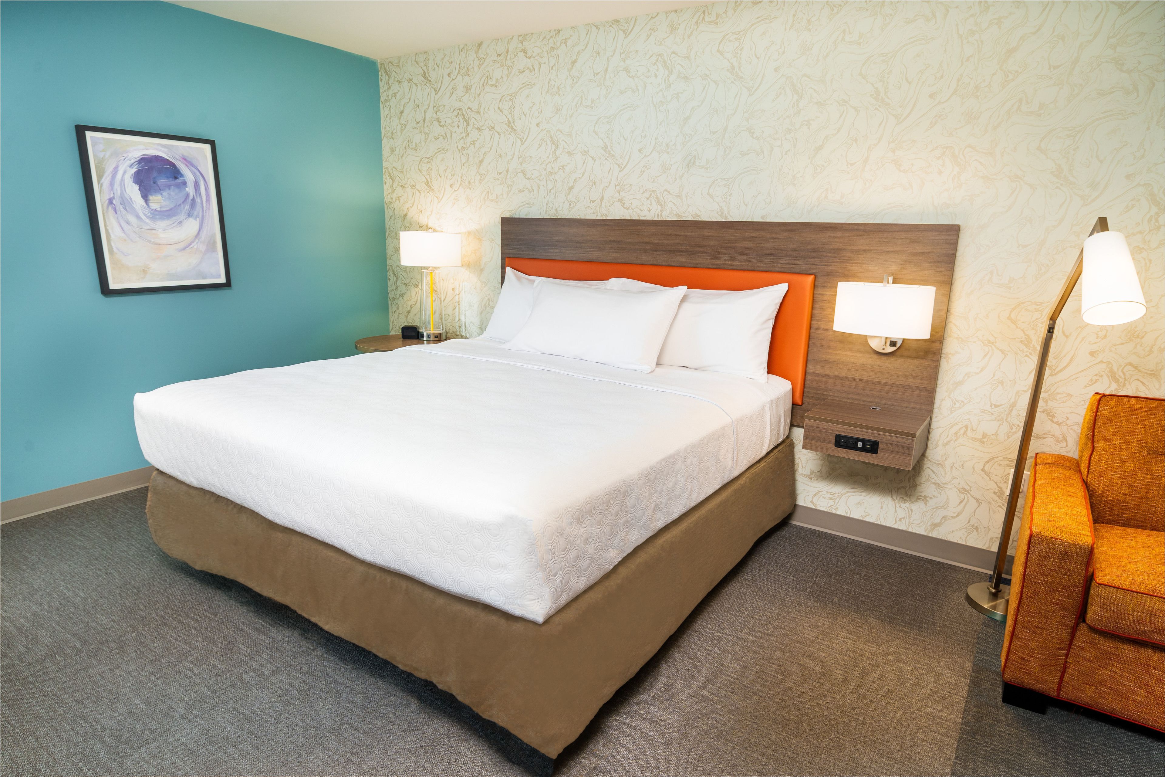 A hotel room with a large bed, two bedside lamps, a nightstand, and a chair.