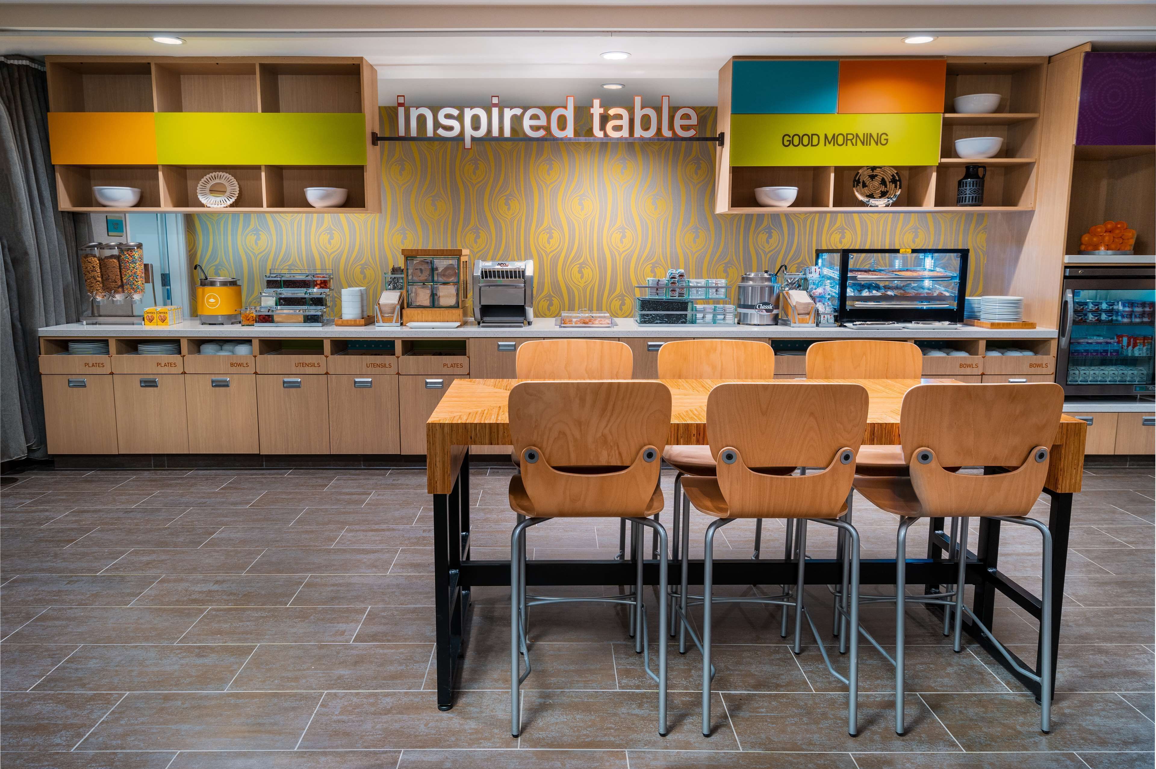 A modern kitchen with a wooden table and chairs, a coffee machine, and a television.