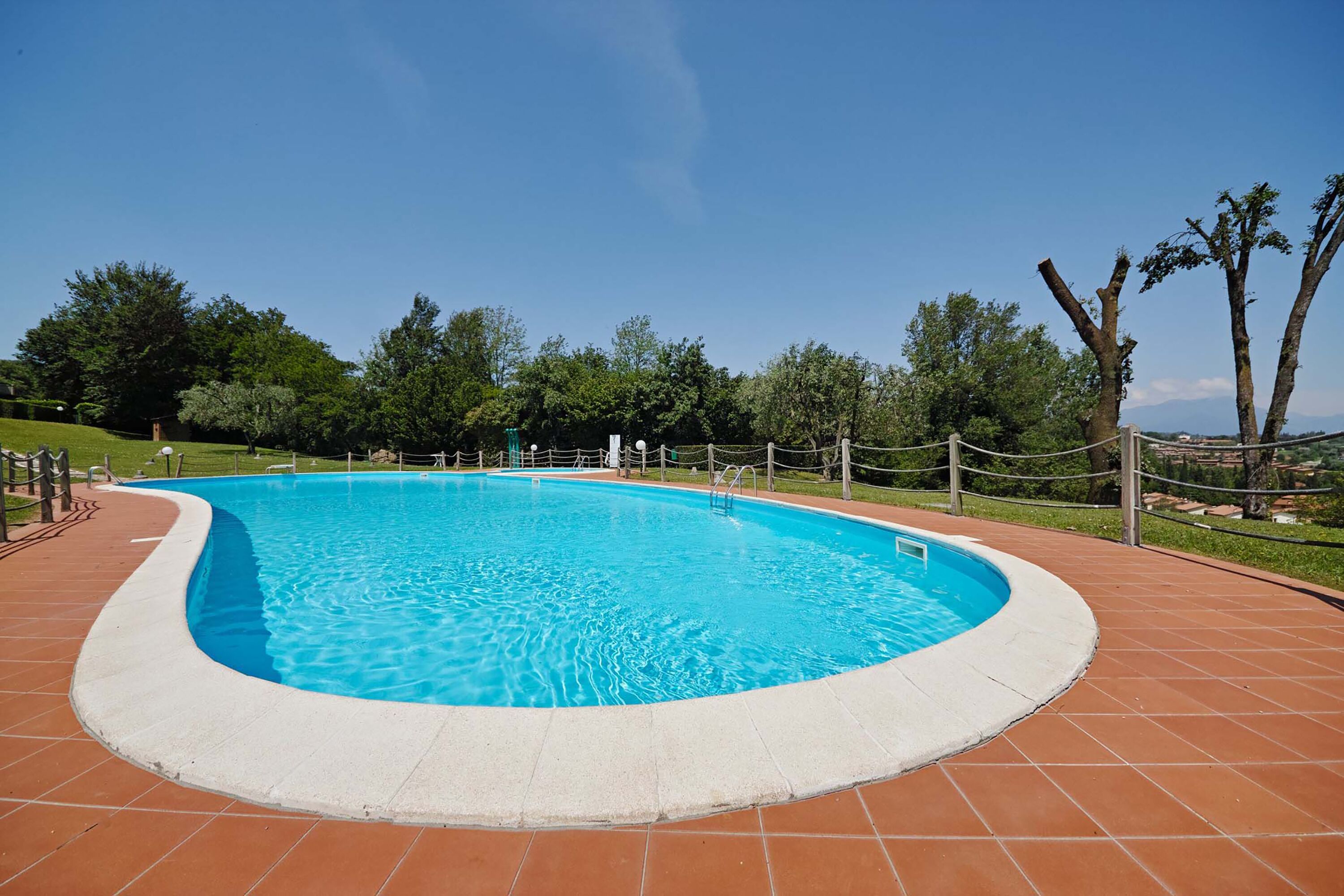 A rectangular swimming pool with a tiled deck surrounding it, enclosed by a fence.