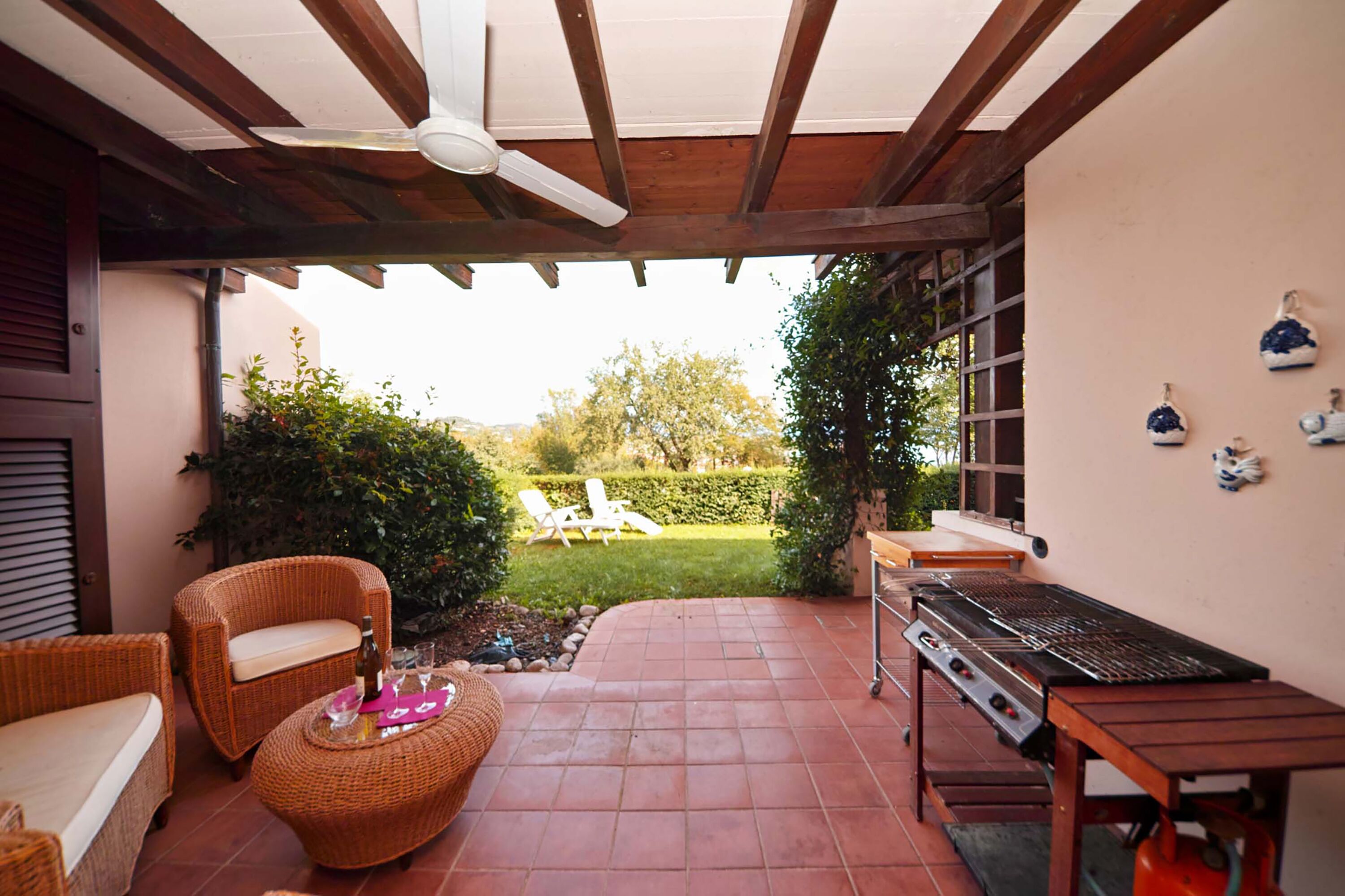 An outdoor patio with wicker furniture, a grill, and a view of the garden.