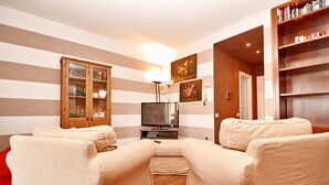 A living room with striped walls, a wooden cabinet, a television, and two beige sofas. - Vista Lago (Padenghe sul Garda)