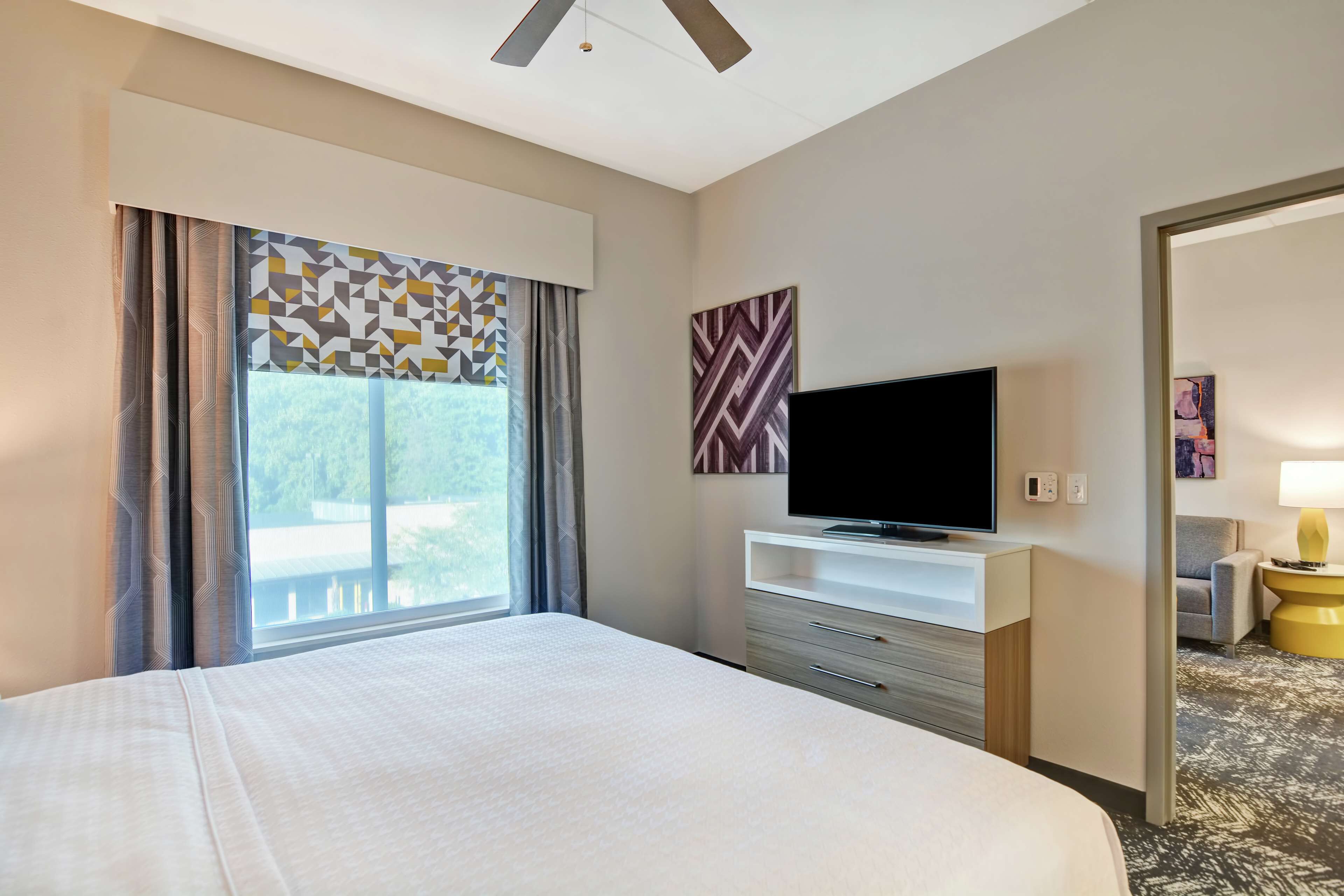 A hotel room with a large bed, a flat-screen TV on a white console, a sofa, and a lamp.