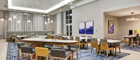 A modern hotel lobby with a large seating area, multiple tables, and ceiling fans.
