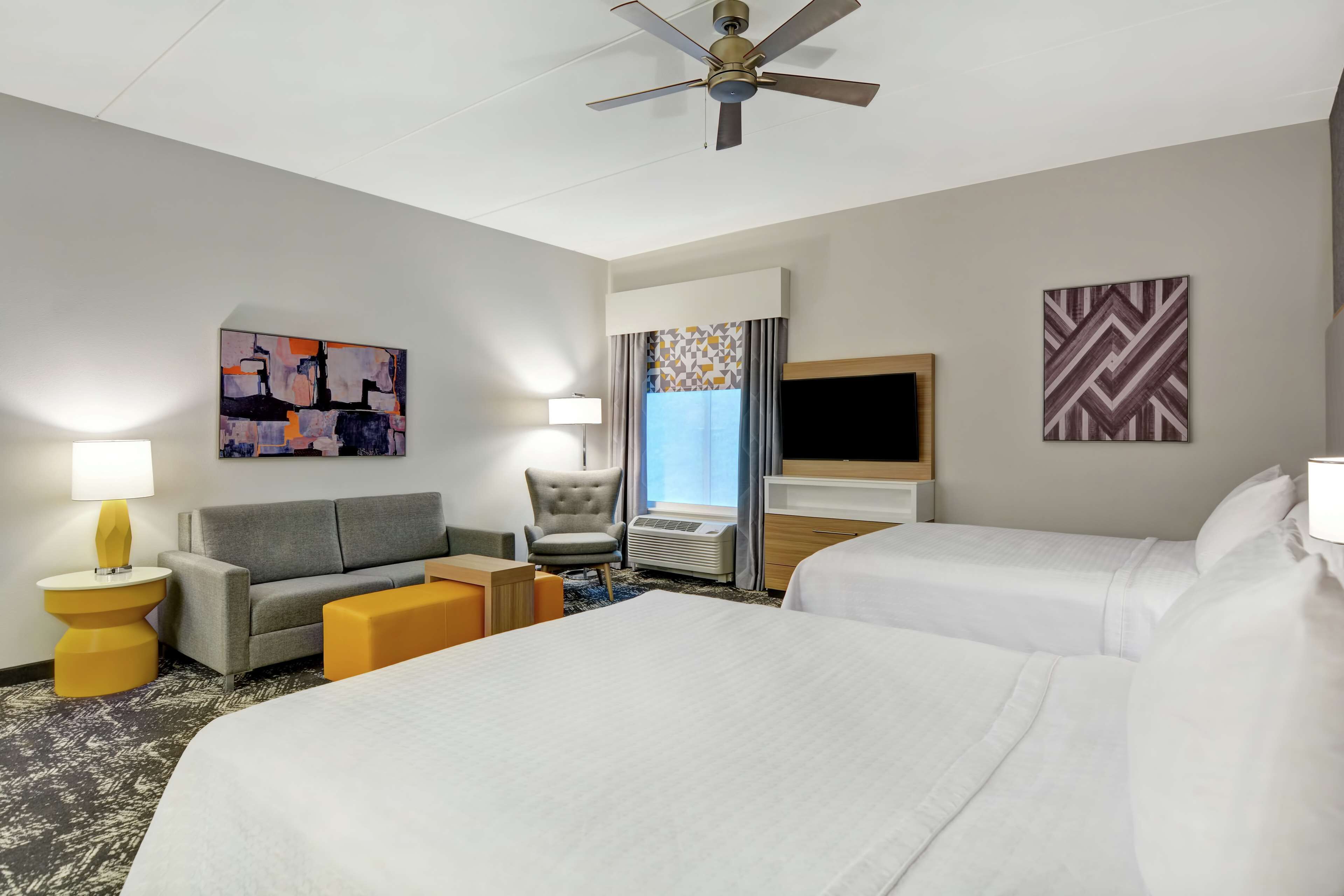 A hotel room with two beds, a sofa, a chair, a TV, and artwork on the walls.