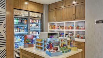 Una cocina de hotel con armarios de madera, un refrigerador lleno de bebidas y una encimera con libros infantiles y aperitivos.