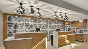 Uma área de recepção com parede estampada em padrão geométrico, balcão de madeira e iluminação pendente.