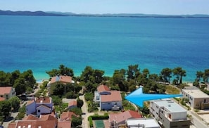 Uma área residencial costeira com casas, mar azul cristalino e uma pequena praia.