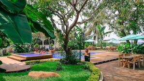 A pool area with a small waterfall, surrounded by lush greenery and wooden seating. - Hostal Las Marias (Taxisco)