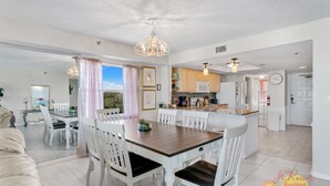 A spacious living area with a dining table, white chairs, and a kitchen in the background.