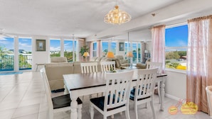 A spacious dining area with a white table and chairs, a chandelier, and a view of the outdoors.