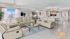 A spacious living room with a beige sofa set, a glass coffee table, and a dining area with a white table and chairs.