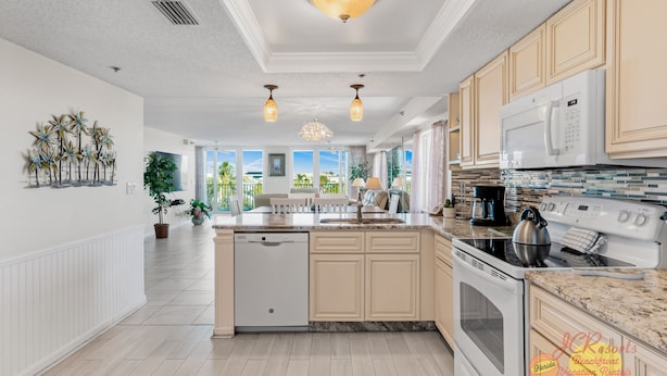 A spacious kitchen with a dishwasher, stove, and microwave. It features light wood cabinets, a granite countertop, and a view of the outdoors.