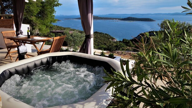 Ein Whirlpool mit Meerblick, ein Tisch mit Stühlen und eine Pergola mit Vorhängen.