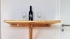 Ein kleiner Holztisch mit zwei Hocker, einer Weinflasche und zwei Gläsern an einer weißen Wand.