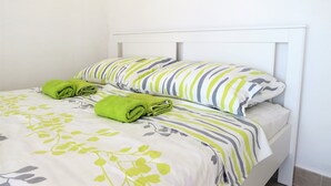 Ein ordentlich bezogenes Bett mit grünen Handtüchern, gestreiften Kissen und einer zudeckenden Tagesdecke mit Blumenmuster.