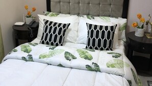 A neatly made bed with a leaf-patterned duvet, a tufted headboard, and two bedside tables with lamps. - A Home Away from Home (Mandaue City)