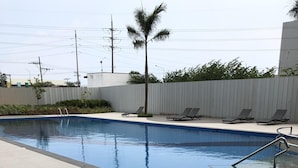 A swimming pool with a tiled deck, a palm tree, and lounge chairs. - A Home Away from Home (Mandaue City)