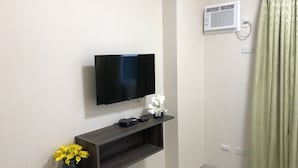 A modern room with a flat-screen TV mounted on the wall, a dark wooden console table with a flower vase, and a green curtain. - A Home Away from Home (Mandaue City)