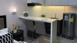 A modern kitchen with white cabinets, a stainless steel refrigerator, a bar counter, and a small dining area with a table and chairs. - A Home Away from Home (Mandaue City)