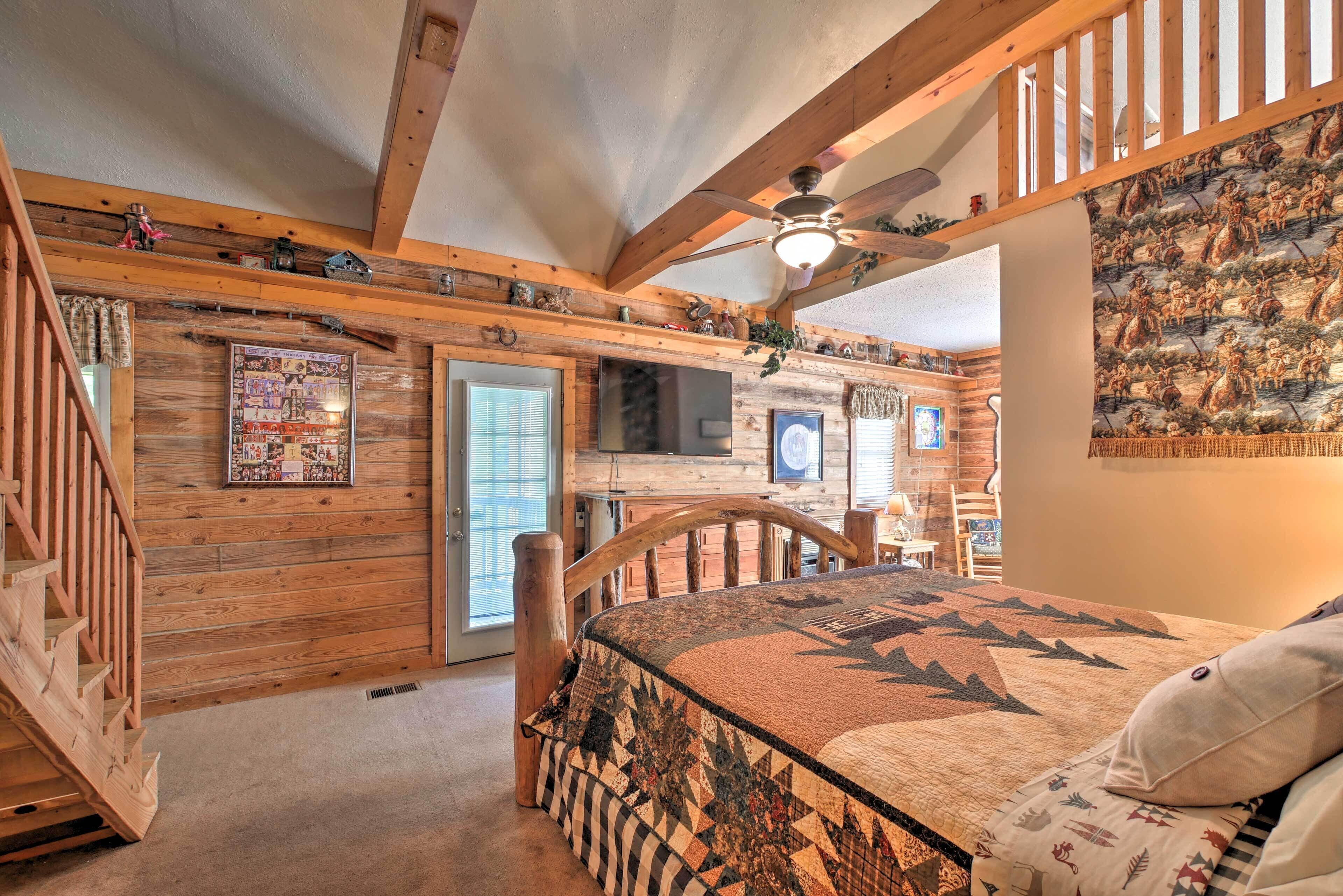 A cozy room with a wooden ceiling, a bed with a patterned bedspread, a ceiling fan, and a mural on the wall.